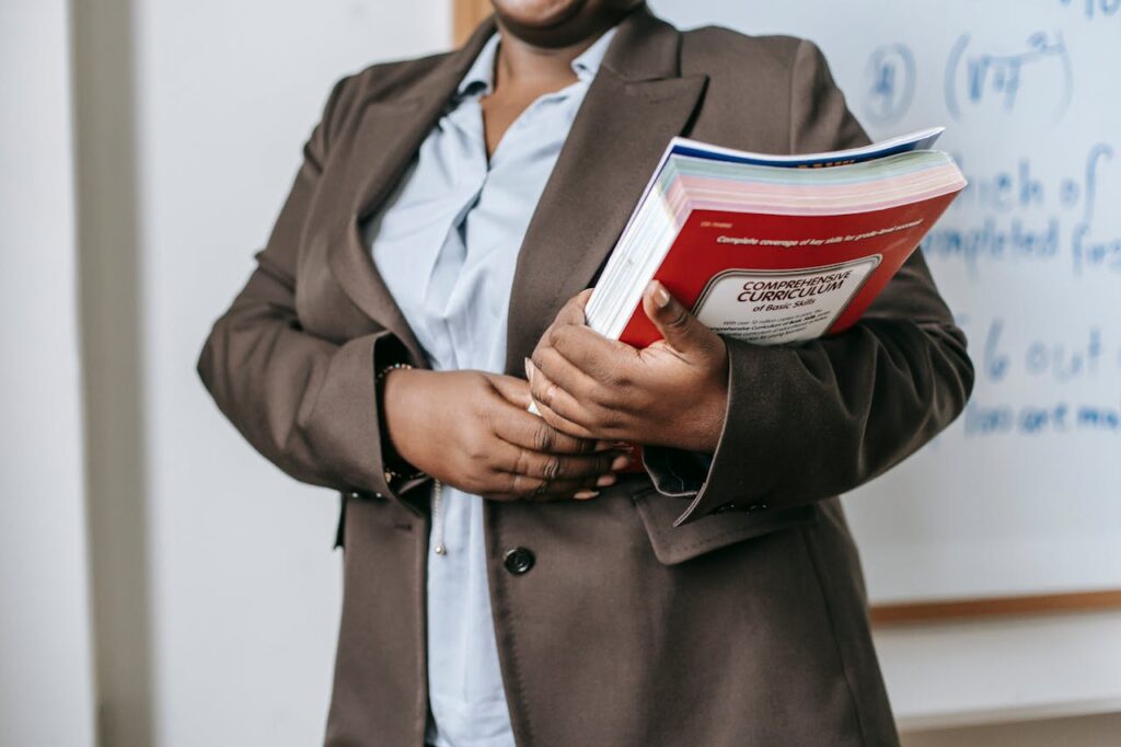 Anonymous black female tutor with books standing near whiteboard at school